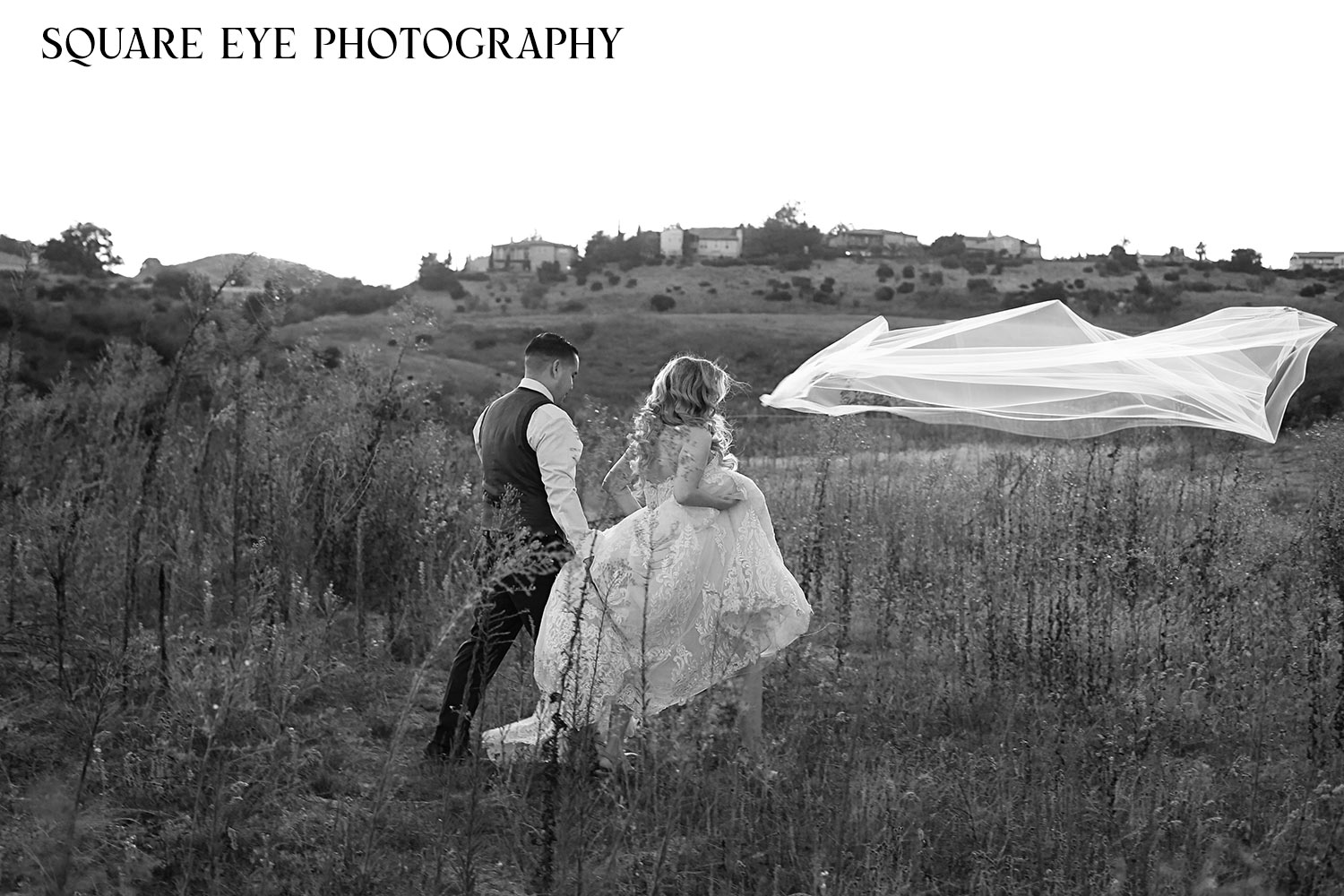 Bride-loses-veil-as-she-is-walking-across-the-field-black-and-white-wedding Bride-loses-veil-as-she-is-walking-across-the-field-black-and-white-wedding