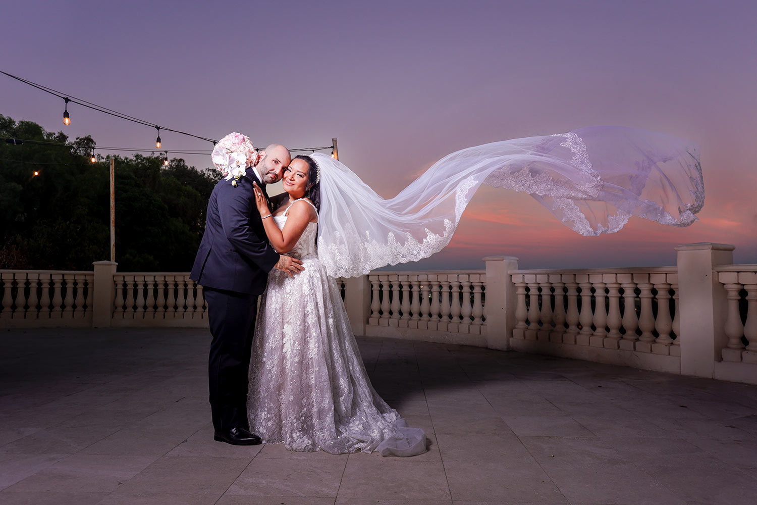 sunset-photography-couple-wedding-veil-tossed "Bride and groom posing together at sunset with a cathedral veil flying behind them during wedding portraits."
